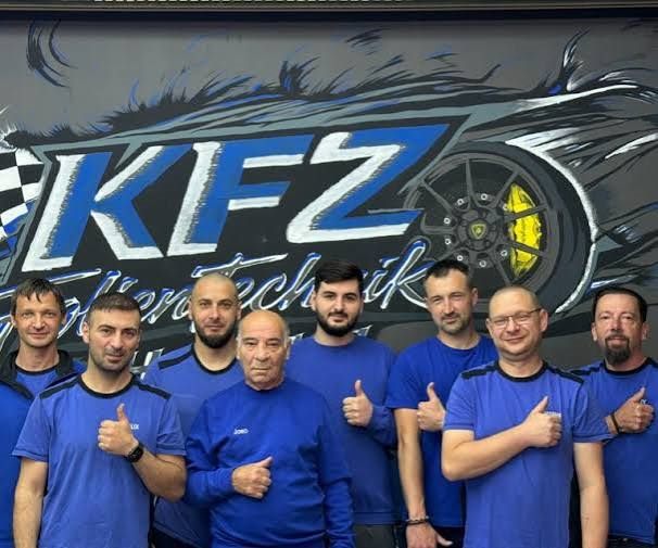 Das Team von KFZ Technik Holhut vor dem Werkstatt-Wandbild