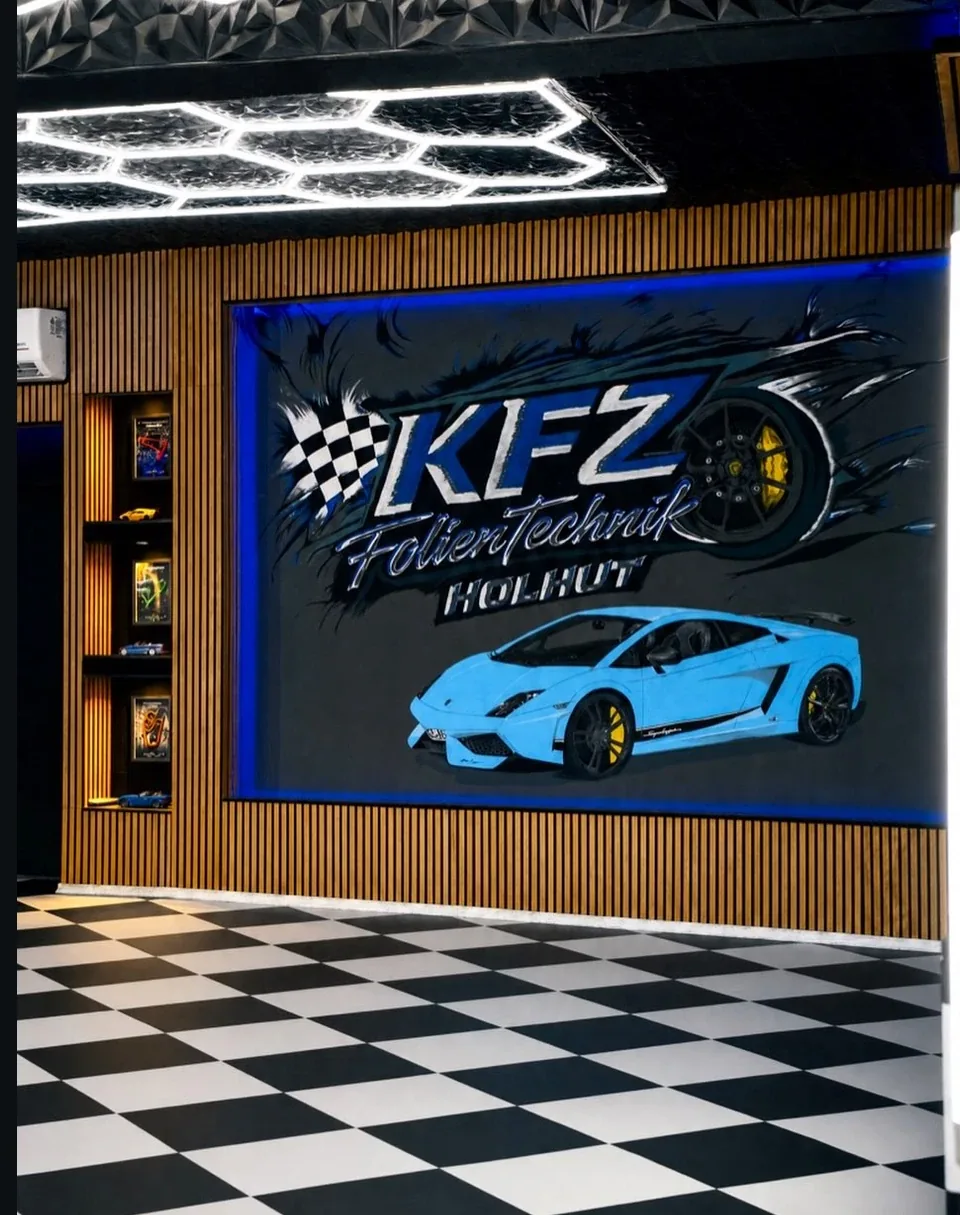 Unser Studio in Bad Staffelstein: Wandbild mit dem Schriftzug KFZ FolienTechnik Holhut und hellblauem Sportwagen, darüber Hexagon-Deckenleuchten, davor Schachbrettboden